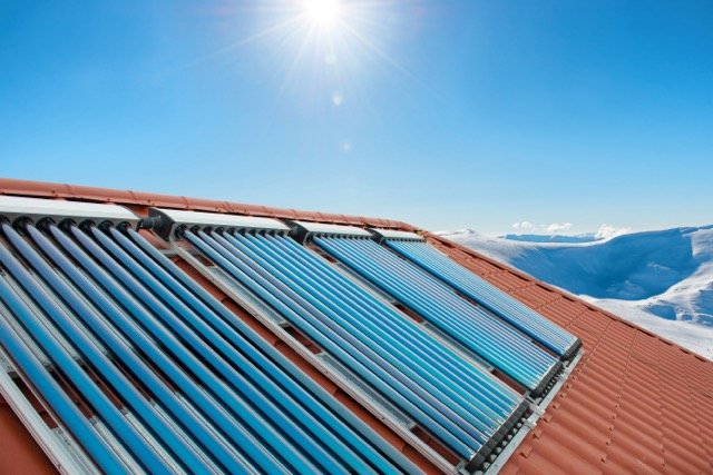 Vacuum collectors - solar water heating tubes on roof of the house with sun and snow mountains